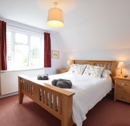 A bedroom with a wooden bed frame bedside tables lamps and a window with red curtains at Hoist Cottage Walberswick