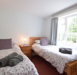 A bedroom with two single beds with floral bedding and grey towels on them at Hoist Cottage Walberswick