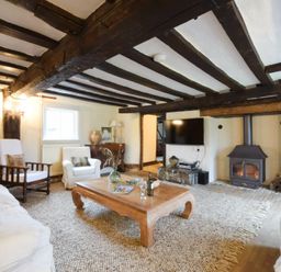 A living room with wooden beams a fireplace and furniture at Church Farmhouse Cookley Near Halesworth