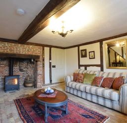 A living room with a striped sofa and cushions a coffee table a rug a wood burning stove in a brick fireplace and framed pictures at Church Farmhouse Cookley Near Halesworth