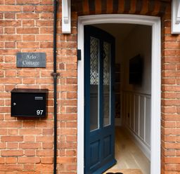 A brick house entrance with a black door partially open a black mailbox with number 97 and a sign saying Arlo Cottage at Arlo Cottage Orford