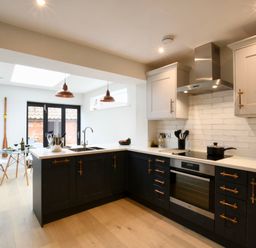 A kitchen with black lower cabinets white upper cabinets and a dining area with glass table and white chairs at Arlo Cottage Orford