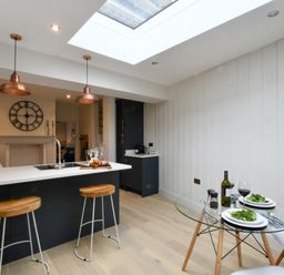 A kitchen with a black island and wooden stools with a glass dining table and two white chairs at Arlo Cottage Orford