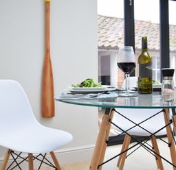 A dining area with a glass table and two white chairs with wooden legs with a bottle of wine wine glasses plates of salad and a salt grinder at Arlo Cottage Orford