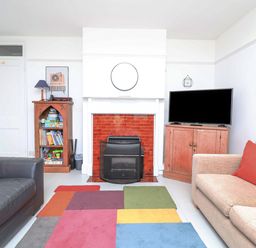 A living room with a fireplace a television on a cabinet and a colorful rug at Time Out Southwold in Southwold