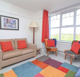 A living room with a beige sofa red pillows two armchairs colorful patchwork rug and a large window at Time Out Southwold in Southwold