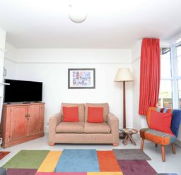 A living room with a sofa and red cushions a multicolored rug and a colorful chair at Time Out Southwold in Southwold