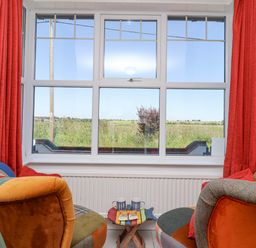 A seating area with two colorful chairs and a small table with mugs in front of a large window with red curtains at Time Out Southwold Southwold