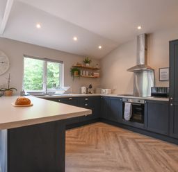 A kitchen with black cabinets wooden shelves and a window at The Piglets in Newbourne Near Woodbridge