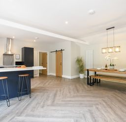 A kitchen with a breakfast bar and stools next to a dining table with bench seating at The Piglets in Newbourne Near Woodbridge
