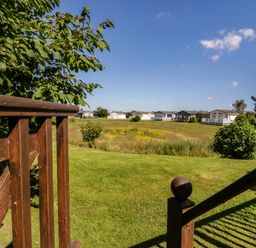 A grassy field with bushes and several small houses in the distance viewed from a wooden deck at The Hide Out in Aldeburgh