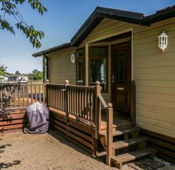 The exterior entrance of a house with wooden steps and railing and a covered grill on a paved area at The Hide Out in Aldeburgh