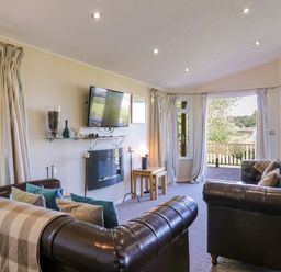 A living room with two leather sofas, a wall-mounted TV, a fireplace, and large windows with curtains at The Hide Out, Aldeburgh