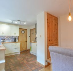 A kitchen with white cabinets and wooden doors and a dining area with upholstered chairs at Chapel Cottage Newbourne Near Woodbridge