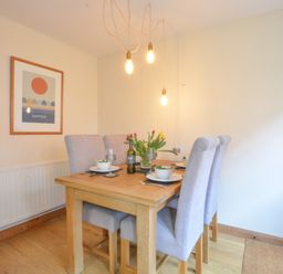 A dining area with a wooden table set for four with gray upholstered chairs and hanging pendant lights at Chapel Cottage Newbourne