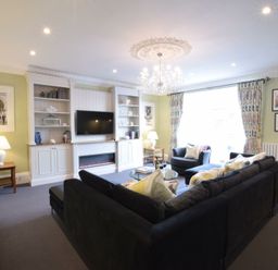 A living room with a black sofa a chandelier and a wall mounted television at Regatta Lookout in Aldeburgh
