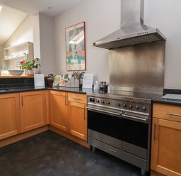 A kitchen with wooden cabinets black countertops a stainless steel stove and range hood at Regatta Lookout in Aldeburgh