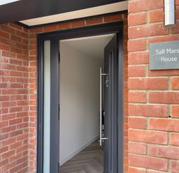 An open black door with a metal handle set in a brick wall next to a sign reading Salt Marsh House in Southwold