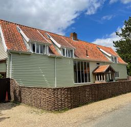 A light green house with a red tile roof and woven wooden fencing along the roadside at Moat Barn in Hasketon Near Woodbridge