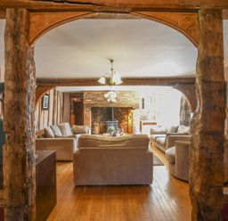 A living room with sofas around a brick fireplace and wooden beams at Moat Barn in Hasketon Near Woodbridge