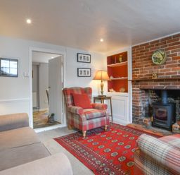 A living room with plaid armchairs a red patterned rug a brick fireplace and lamps at 17 South Green Southwold