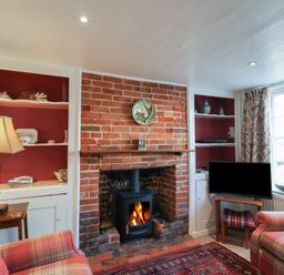 A living room with a brick fireplace wood stove armchairs a lamp bookshelf TV and window at 17 South Green Southwold