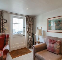 A sitting room with plaid armchair and sofa near a door and window with patterned curtains at 17 South Green Southwold