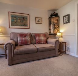 A living room with a sofa and two side tables with lamps and framed pictures on the walls at 17 South Green Southwold