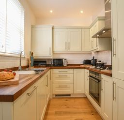 A kitchen with wooden countertops white cabinets a loaf of bread on a cutting board and appliances at The Gallery Blythburgh near Southwold