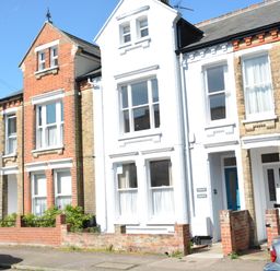 A street view of attached brick and white painted houses with cars parked outside at Driftwood Southwold