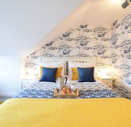 A bedroom with a bed with blue and yellow pillows and a tray with breakfast items Driftwood Southwold