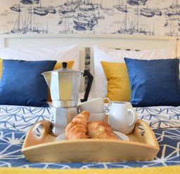 A tray with a coffee pot croissants cups and a jug on a bed with blue and yellow cushions at Driftwood Southwold