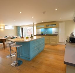 A kitchen with a blue island and beige cabinets next to a dining table with blue and white chairs at Tamarisk Aldeburgh in Aldeburgh
