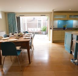A dining area with a wooden table set for six people next to an open kitchen and patio at Tamarisk Aldeburgh in Aldeburgh