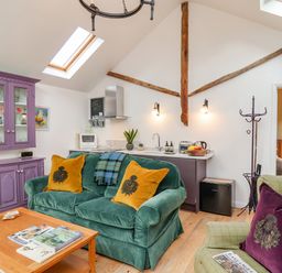 A living area with green and purple couches, a purple cabinet, a wooden coffee table, and a kitchen counter at The Bothy at Snape Hall in Snape Suffolk