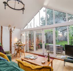 A living room with large glass doors opening to a garden with outdoor furniture at The Bothy at Snape Hall in Snape Suffolk