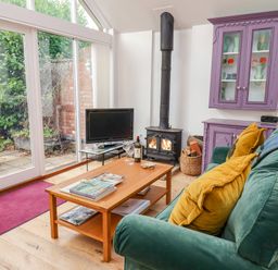 A living room with a green sofa yellow pillows a wooden coffee table a wood-burning stove and purple cabinet at The Bothy at Snape Hall in Snape Suffolk