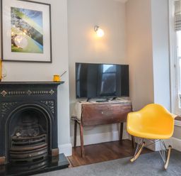 A yellow chair next to a window and a television on a wooden table beside a black fireplace at Osprey in Southwold