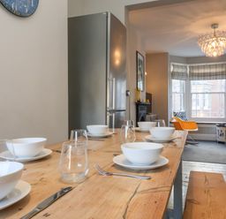 A dining table set with white bowls and glasses in a room with a window seat and an orange chair at Osprey in Southwold
