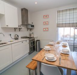 A kitchen with white cabinets a wooden dining table set with bowls and cutlery at Osprey in Southwold