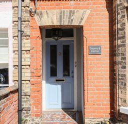 A blue front door numbered 3 with a tiled entrance and a sign reading Osprey and Kestrel at a brick building in Southwold