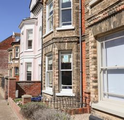 A row of brick and painted houses with bay windows and small front gardens on a residential street