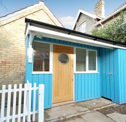 A small blue wooden building with a round window door and white fence at Garden Cottage Southwold