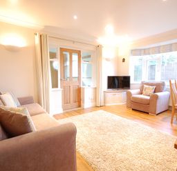 A living room with two sofas a television on a cabinet a dining table and chairs and a door with windows at Garden Cottage Southwold