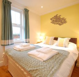 A bedroom with a double bed two bedside tables with lamps and a window with curtains at Garden Cottage Southwold