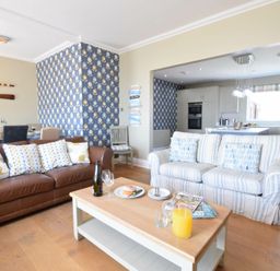 A living room with two sofas a wooden coffee table and a dining area with oars on the wall at St Marys View Southwold