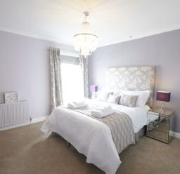 A bedroom with a double bed bedside tables with lamps curtains and a chandelier at St Marys View Southwold