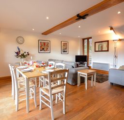 A dining area with a table set for six and a living area with two sofas and a TV at Three Chantry Barns Orford