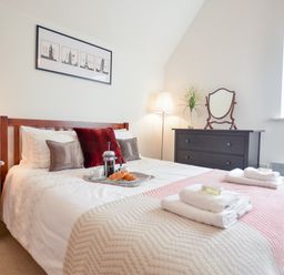 A bedroom with a bed with pillows and a tray with breakfast items next to a wooden nightstand and a dark dresser with a mirror at Three Chantry Barns in Orford