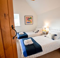 A bedroom with two single beds with striped bedding a bedside table with a lamp and orange juice and a colorful framed picture on the wall at Three Chantry Barns Orford